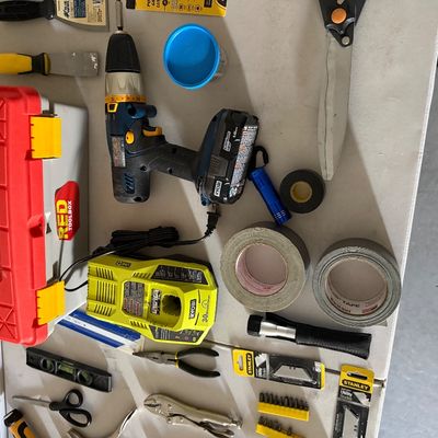 Sale Photo Thumbnail #83: Assortment of hand tools and household hardware, featuring a Ryobi cordless drill with battery charger, a Red Toolbox, rolls of duct tape, pliers, levels, and replacement blades.