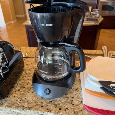 Sale Photo Thumbnail #202: Black Mr. Coffee 12-cup drip coffee maker with glass carafe sitting on a kitchen countertop.