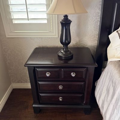 Sale Photo Thumbnail #21: Dark wood three-drawer nightstand with silver-tone hardware, topped with a dark urn-style table lamp.
