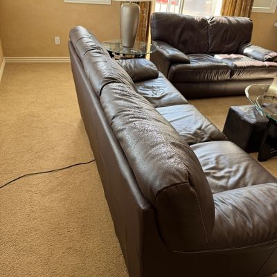 Sale Photo Thumbnail #229: Contemporary dark brown leather sofa set featuring a long three-cushion couch and a matching loveseat, displaying light wear and creasing on the seating surfaces.