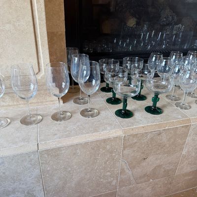 Sale Photo Thumbnail #40: Collection of glass drinkware, including clear wine glasses and novel cactus-stem margarita glasses, displayed on a tiled hearth.