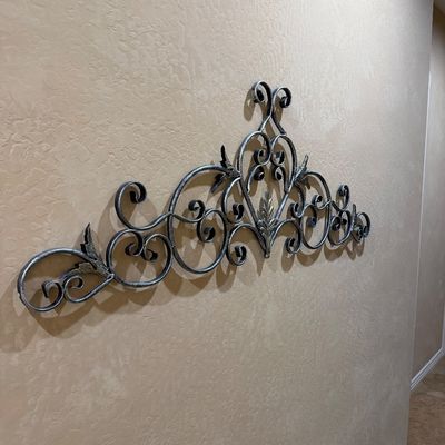 Sale Photo Thumbnail #156: Large scrollwork wrought iron wall pedicure with silver-gray finish and leaf accents mounted above a hallway wall.