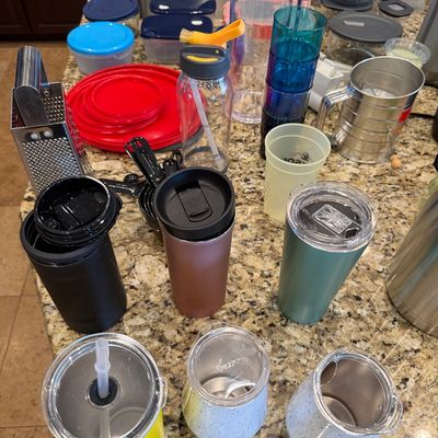 Sale Photo Thumbnail #168: Assortment of modern kitchenware including stainless steel travel tumblers, plastic food storage containers, water bottles, and a box grater arranged on a granite countertop.