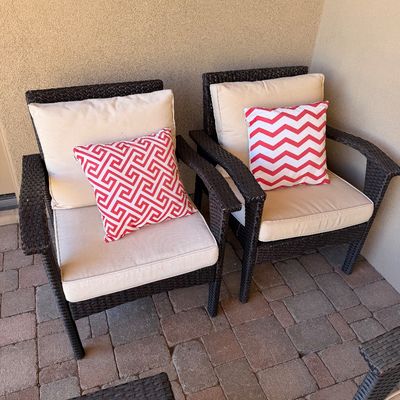 Sale Photo Thumbnail #250: Pair of dark brown resin wicker outdoor armchairs with off-white seat cushions and red-and-white patterned accent pillows.