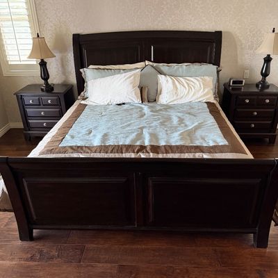 Sale Photo Thumbnail #18: Dark wood sleigh bed frame with matching panel headboard and footboard, flanked by two matching three-drawer nightstands topped with table lamps.