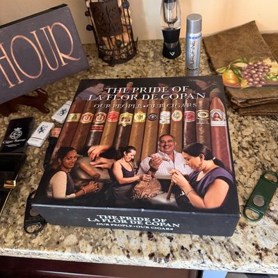 Sale Photo Thumbnail #49: Large "The Pride of La Flor de Copan" cigar box set presented on a granite countertop alongside cigar accessories, butane refill, and wine cork display.