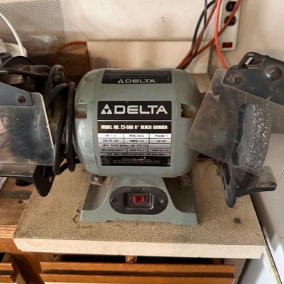 Sale Photo Thumbnail #61: Delta Model 23-580 6-inch bench grinder with dual eye shields, mounted on a workbench surface.
