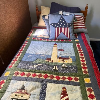 Sale Photo Thumbnail #116: Twin bed featuring a wooden spindle frame topped with a lighthouse-themed patchwork quilt and patriotic throw pillows.