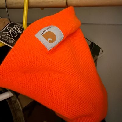Sale Photo Thumbnail #124: Bright orange Carhartt knit beanie, hanging on a clothes hanger with original tags attached.