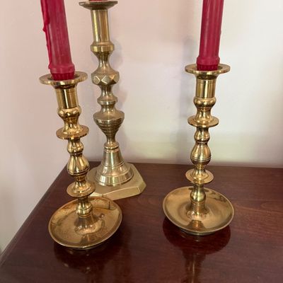 Sale Photo Thumbnail #25: Trio of polished brass candlestick holders in traditional turned-baluster styles, holding red taper candles.