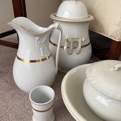 Sale Photo Thumbnail #45: Antique white porcelain wash set including a pitcher, small tumbler, covered jar, and wash basin, all accented with thin gold trim lines.