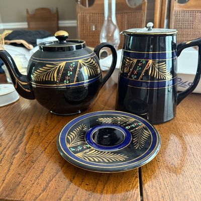 Sale Photo Thumbnail #170: Vintage Staffordshire black porcelain tea service pieces featuring hand-painted gold leaf motifs, cobalt blue bands, and enameled dot accents on English redware..