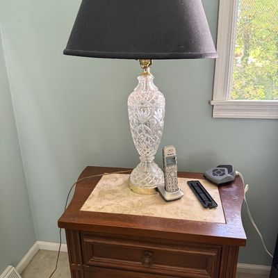 Sale Photo Thumbnail #19: Traditional cut crystal table lamp with a dark fabric shade, displayed on a wooden nightstand with mesh-insert cabinet doors.