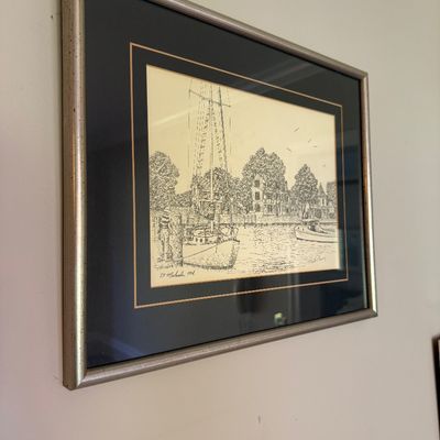 Sale Photo Thumbnail #52: Framed ink drawing titled 'St. Michaels, MD', depicting a sailboat docked near coastal buildings. Presented in a black double mat with gold trim inside a silver-finished wooden frame.