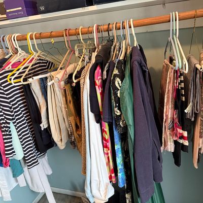 Sale Photo Thumbnail #105: Closet full of women's clothing on hangers, including striped tops, jackets, scarves, and pants beneath stacked shoe boxes.