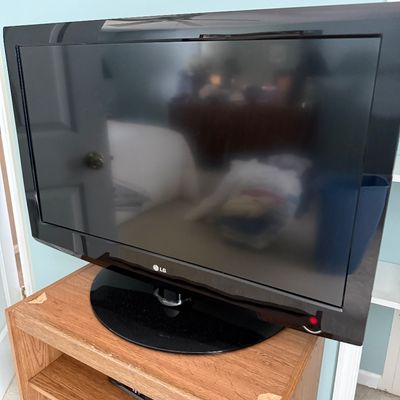 Sale Photo Thumbnail #107: Black LG flat-screen LCD television mounted on a oval swivel base, sitting atop a wooden media stand.