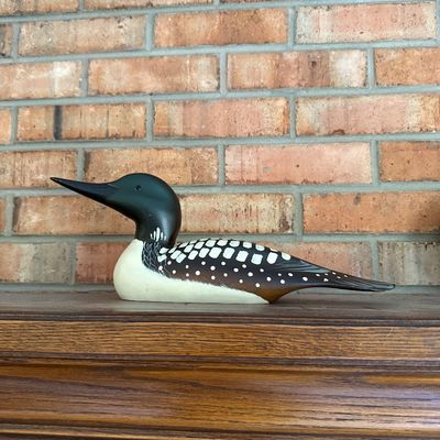 Sale Photo Thumbnail #40: Hand-carved and painted wooden loon decoy, featuring detailed feather patterns on a dark and white body, displayed on a wooden fireplace mantel.