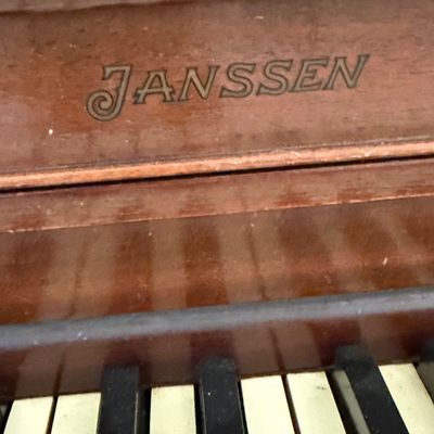 Sale Photo Thumbnail #37: Janssen brand upright piano with a mahogany finish, showing the maker's mark above the keys.