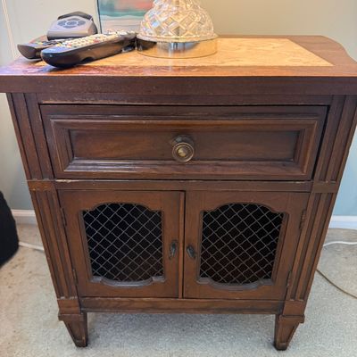 Sale Photo Thumbnail #110: Vintage dark wood nightstand with a single drawer, mesh cabinet doors, and an inlaid marble or faux-marble top surface.
