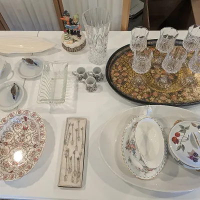 Collection of tabletop glassware and porcelain items, including crystal stemware on a decorative tray, a porcelain gravy boat, floral...