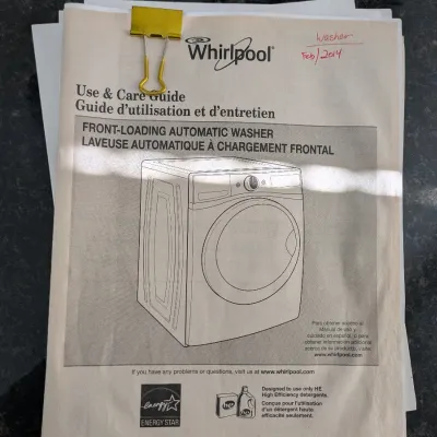 Whirlpool front-loading automatic washer Use & Care Guide booklet clipped with a yellow binder clip, handwritten date of Feb 2014 in...