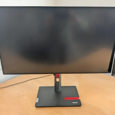 Lenovo ThinkVision flat-panel computer monitor with an adjustable stand featuring red accents, sitting on a wooden desk.