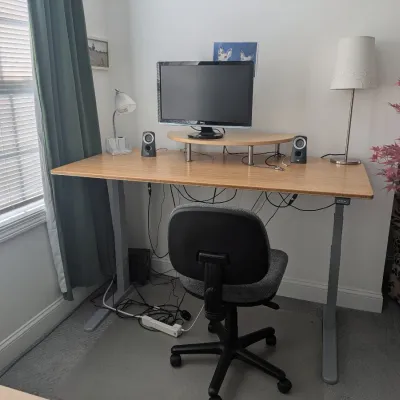 Modern adjustable standing desk with bamboo-style top, monitor stand, and grey metal base, paired with a grey fabric task chair.