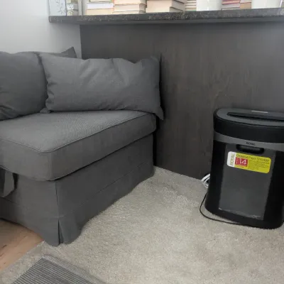 A grey upholstered convertible ottoman seat with matching throw pillows, and a Royal crosscut paper shredder.