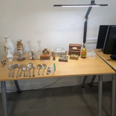 Collection of decorative tabletop items including silver-tone serving flatware, porcelain vases, tea cups, glass candlesticks, trinket...