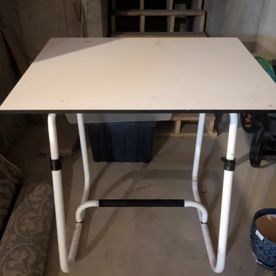 White height-adjustable utility table with tubular metal frame, featuring minor surface wear.
