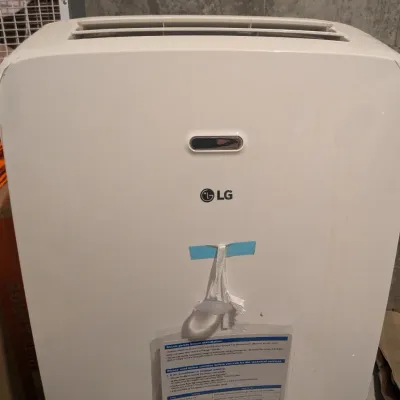 LG portable air conditioner unit in modern white casing, featuring an attached remote control and front display window.
