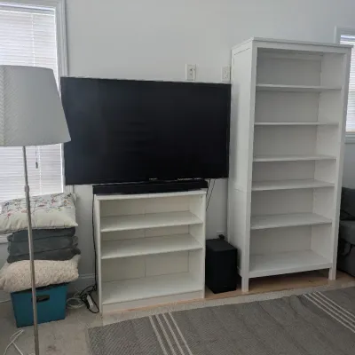 Modern entertainment setup including a large flat-screen television resting on a low white bookcase alongside a tall matching white...