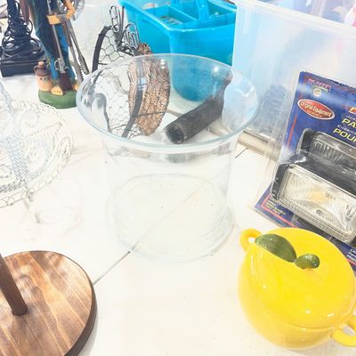 Sale Photo Thumbnail #93: Collection of eclectic household goods, featuring a clear glass hurricane vase, a yellow ceramic apple-shaped dish, a wizard figurine, and packaged automotive fog lights.