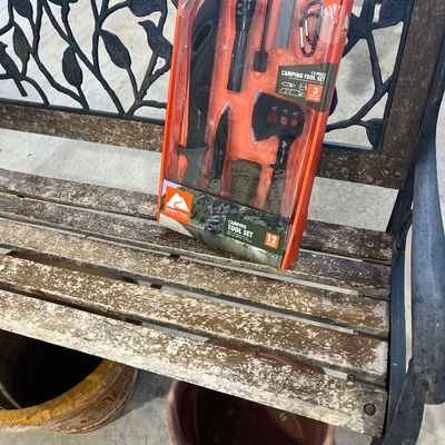 Sale Photo Thumbnail #3: Ozark Trail 12-piece camping tool set in original orange packaging resting on a weathered wooden park bench with cast iron sides.