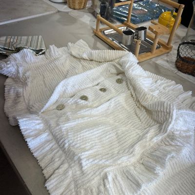 Sale Photo Thumbnail #64: White ribbed chenille or corduroy blanket featuring ruffled edges and decorative buttons, displayed alongside various household goods on a folding table.