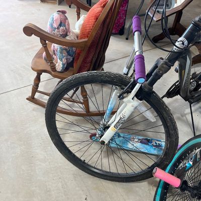 Sale Photo Thumbnail #26: Mongoose bicycle with purple handlebar grips, displayed alongside a children's Frozen scooter and a vintage wooden rocking chair.