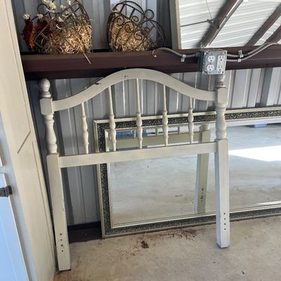Sale Photo Thumbnail #74: White painted wooden spindle headboard resting on a concrete floor alongside large framed wall mirrors and decorative wire baskets.
