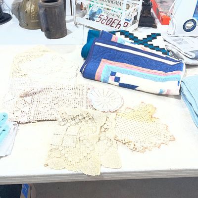 Sale Photo Thumbnail #117: Collection of vintage handmade crocheted lace doilies and folded colorful patchwork quilts displayed on a folding table.
