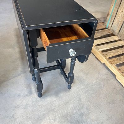 Sale Photo Thumbnail #131: Black painted drop-leaf console table featuring turned legs, a single drawer with a glass knob, and a distressed finish.