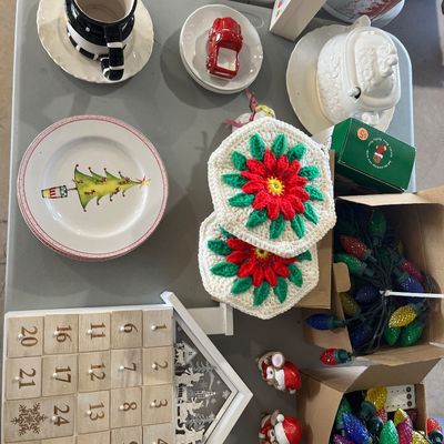 Sale Photo Thumbnail #35: Collection of holiday decor and tableware, including a wooden advent calendar, crocheted poinsettia potholders, Christmas tree design plates, string lights, and small porcelain figurines.