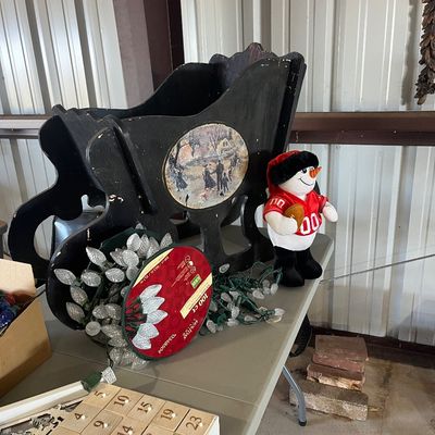 Sale Photo Thumbnail #85: Collection of holiday decorations, including a black wooden sleigh display, a plush football snowman, C9 LED Christmas light strands, and a wooden advent calendar.