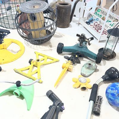 Sale Photo Thumbnail #24: Collection of vintage and modern lawn care items, including various lawn sprinklers, hose nozzles, and bird feeders arranged on a table.