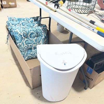 Sale Photo Thumbnail #27: Collection of household goods including blue and white floral outdoor cushions, a white plastic trash can, and various tools on folding tables.