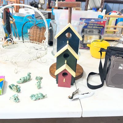 Sale Photo Thumbnail #104: Rustic painted wooden birdhouse tree stands alongside small ceramic figurines, a vintage portable radio, and decorative housewares on a table.