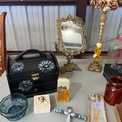 Sale Photo Thumbnail #28: Collection of vintage vanity items, featuring an ornate brass tabletop mirror, a floral-trimmed lamp, painted wooden jewelry boxes, and decorative glassware.
