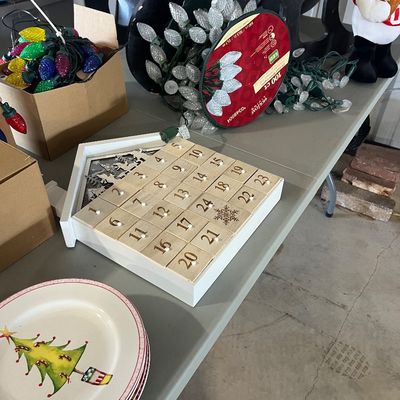Sale Photo Thumbnail #84: Collection of Christmas decorations including a wooden advent calendar box, string lights in boxes, and holiday-themed ceramic dinner plates.