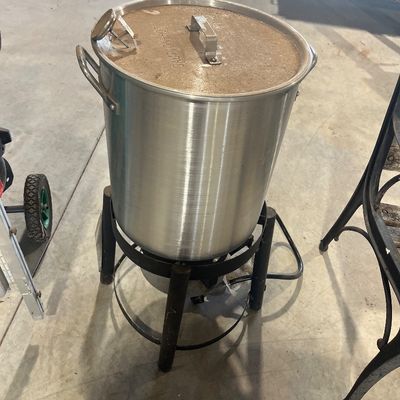 Sale Photo Thumbnail #90: Outdoor propane turkey fryer with a large aluminum stockpot, lid, thermometer, and black metal burner stand.