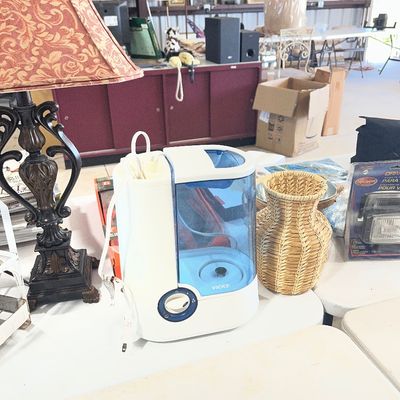 Sale Photo Thumbnail #67: Vicks cool mist humidifier displayed on a table alongside an ornate dark metal lamp with a patterned shade and a woven wicker vase.