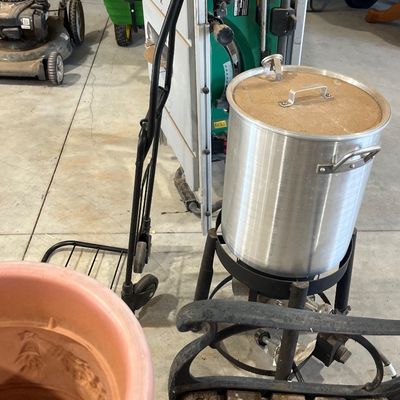 Sale Photo Thumbnail #4: Large outdoor aluminum turkey fryer pot with burner stand, displayed alongside lawn care tools, a hand truck, and garage items.