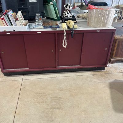 Sale Photo Thumbnail #70: Large maroon sliding-door storage cabinet topped with various household items, including a flat-screen television, vintage telephones, books, and a lamp shade.